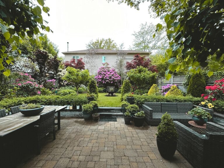 A tranquil backyard garden showcasing vibrant flowers, lush greenery, and patio furniture.