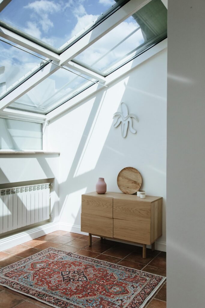 pexels-photo-10222712-10222712 Bright attic room featuring skylight, dresser, and patterned carpet under sunlight.