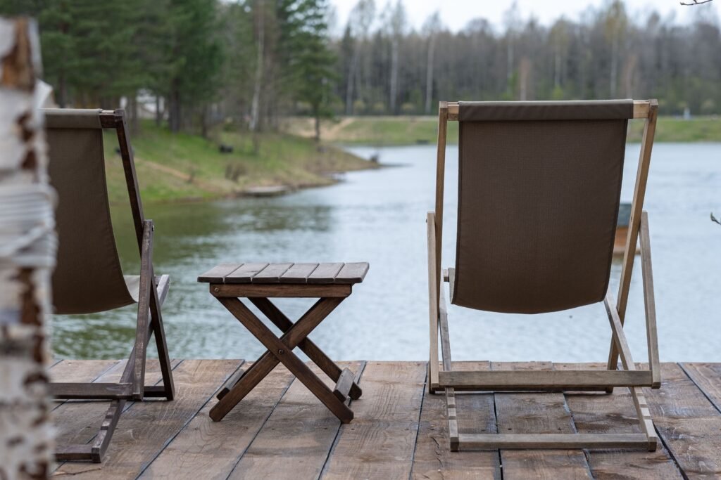 pexels-photo-12236090-12236090 Rustic wooden deck chairs and table overlooking a serene lake and landscape.
