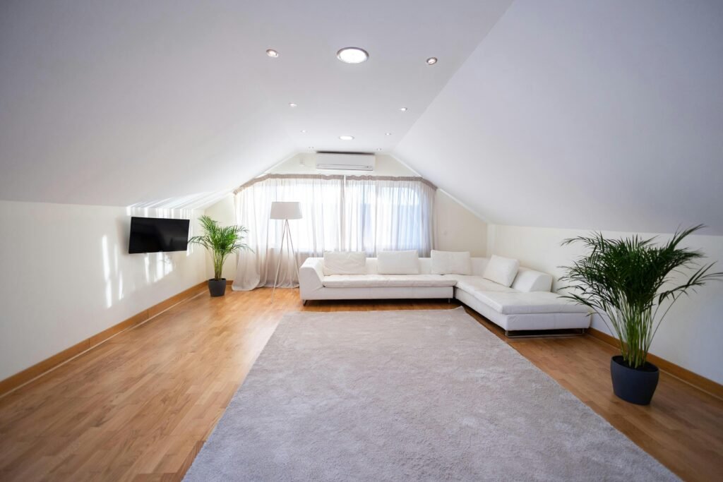 pexels-photo-30211363-30211363 Spacious attic living room with white sofa, hardwood floor, and modern decor.