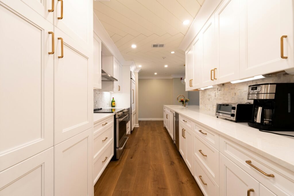 Bright modern kitchen with white cabinets, wooden floor, and appliances.