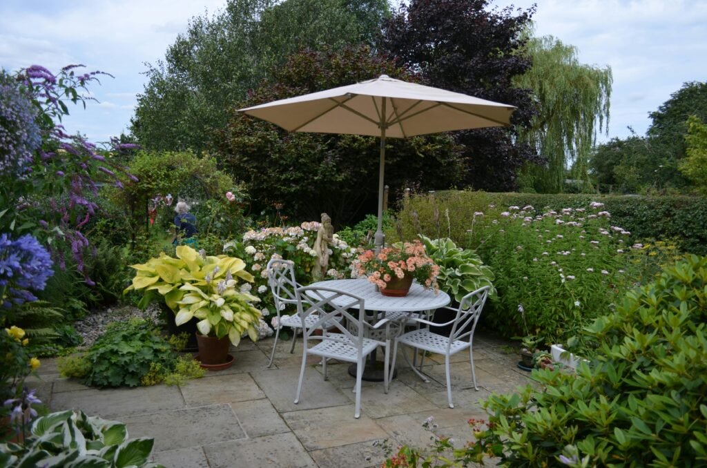 A serene garden patio featuring a table with chairs, umbrella, and vibrant flowers in full bloom.