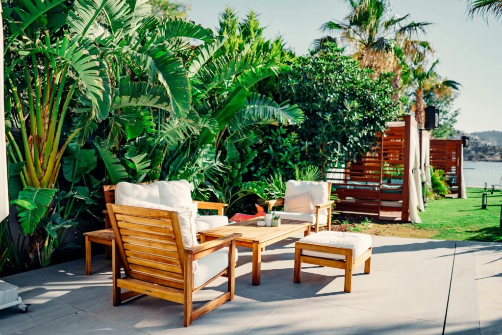 pexels-photo-7969008-7969008 Relaxing outdoor patio with wooden furniture surrounded by lush greenery and tropical plants.