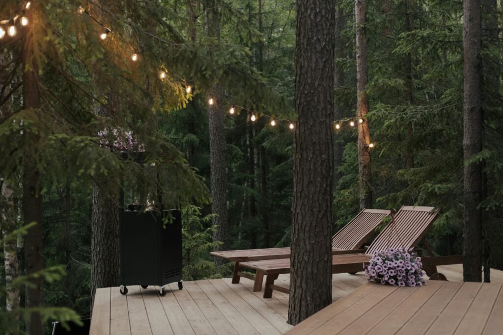 pexels-photo-8845127-8845127 A peaceful forest scene featuring a wooden deck, sun loungers, and string lights.